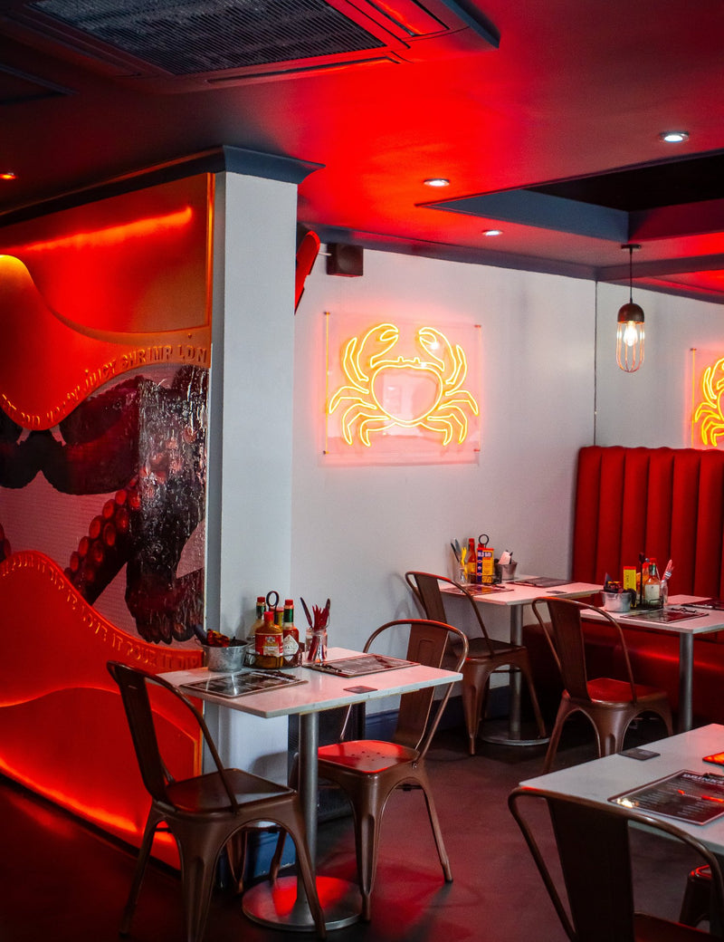 Hot n Juicy Shrimp LDN Dulwich branch with red leather sofa, LED crab sign, copper chairs, and a vibrant artwork feature wall.