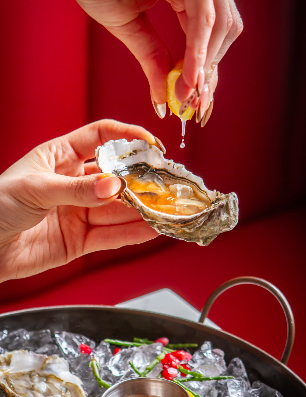 Woman squeezing fresh lemon over an oyster, preparing to enjoy a seafood dish.